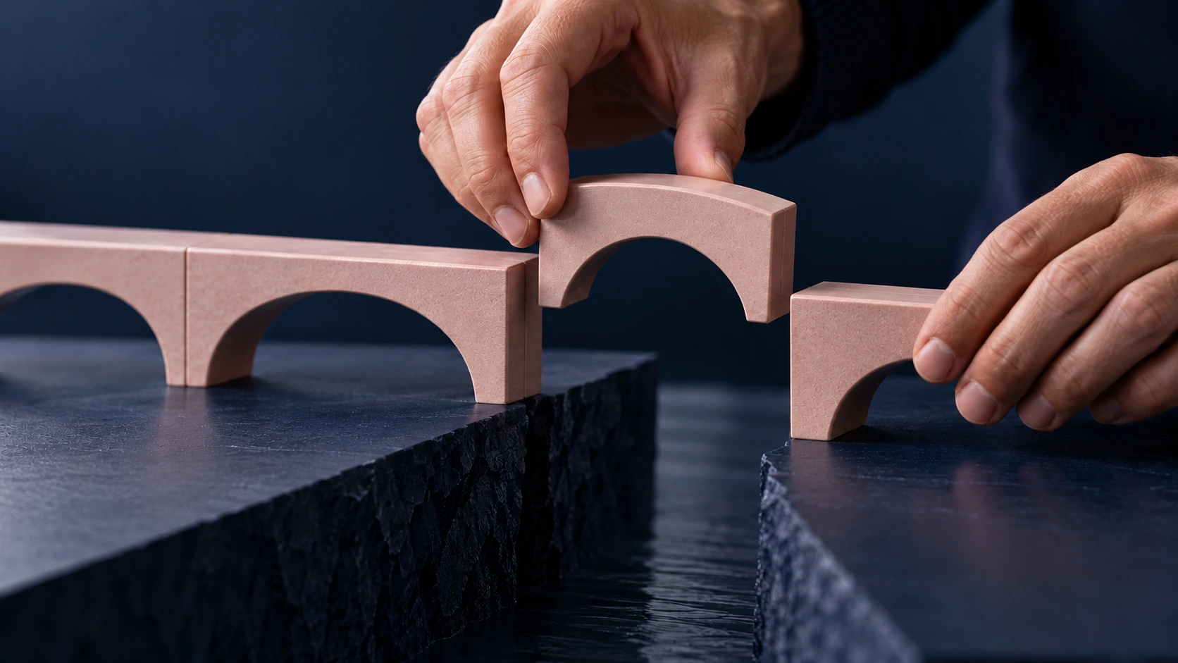 Hands placing the final arch piece to complete a bridge between two separated surfaces